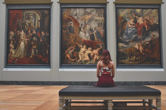 Jeune femme rousse assise devant trois tableaux classiques dans un musée